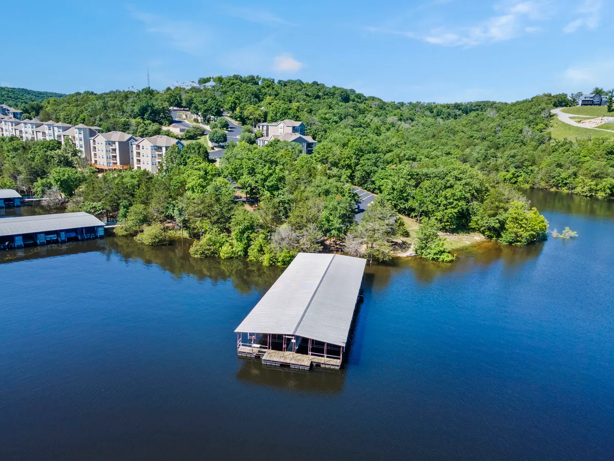 A serene lakefront with a boat dock extending over calm water, bordered by lush greenery and residential buildings. The quiet mood invites guests to unwind, fish, or set off for a boating adventure.