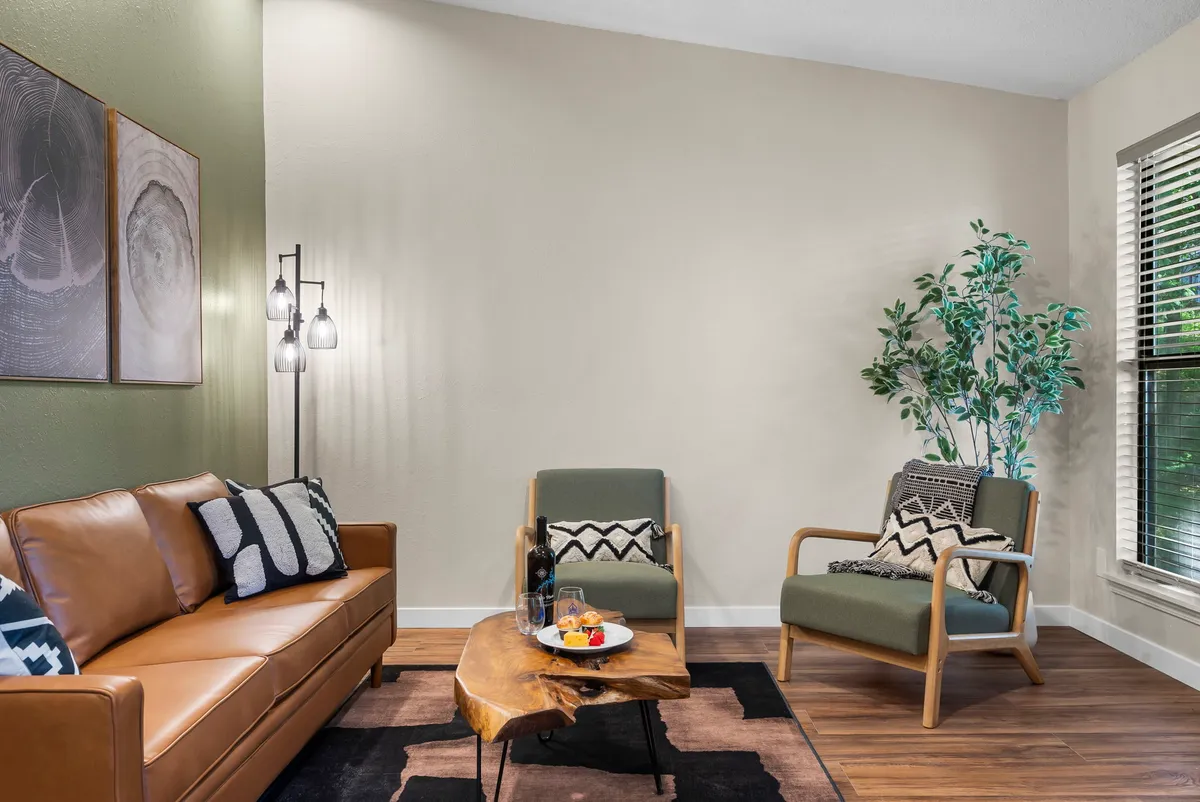 A welcoming interior scene featuring a brown leather sofa, wooden coffee table, green chairs, wall art, and a vibrant houseplant. The room exudes warmth and is well-lit, offering ample space for family activities while keeping pets close.