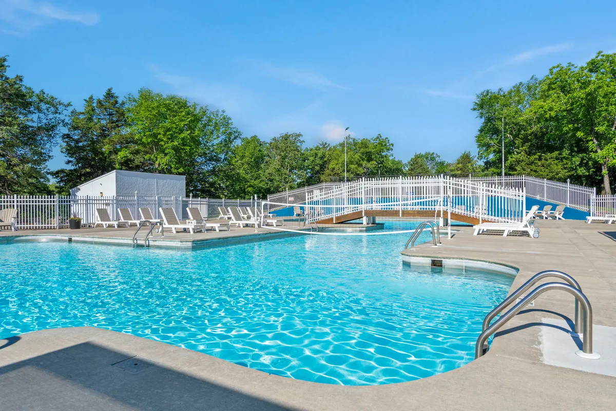 A vibrant outdoor swimming pool scene featuring a wooden bridge, inviting lounge chairs, and lush greenery surrounding the pool. The setting is designed for both family relaxation and playful gatherings under the sun.