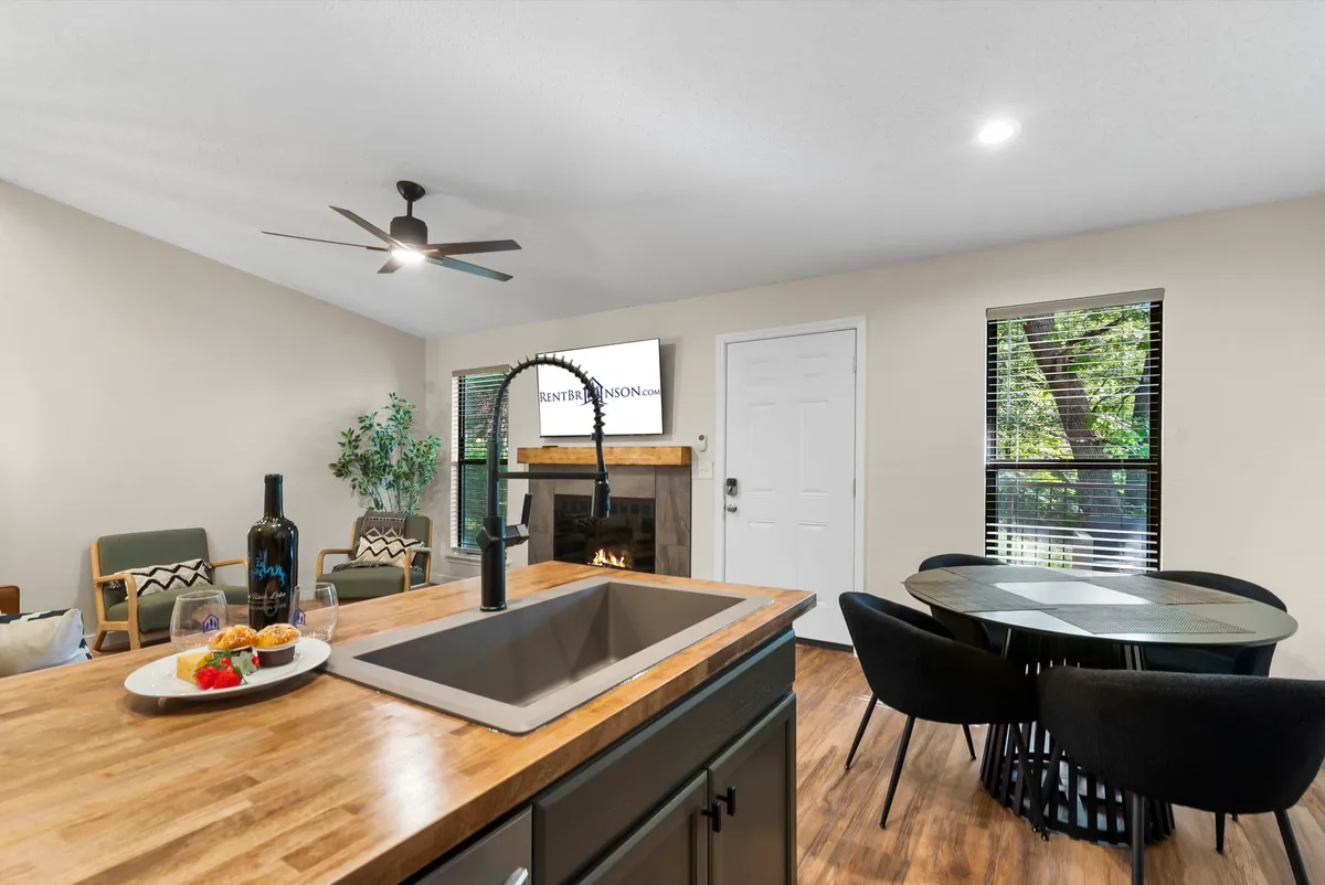 A bright, inviting interior where the kitchen sink, dining table, and fireplace are visible in a seamless layout. Comfortable seating and soft lighting suggest an environment ideal for cooking, entertaining, and relaxing together.
