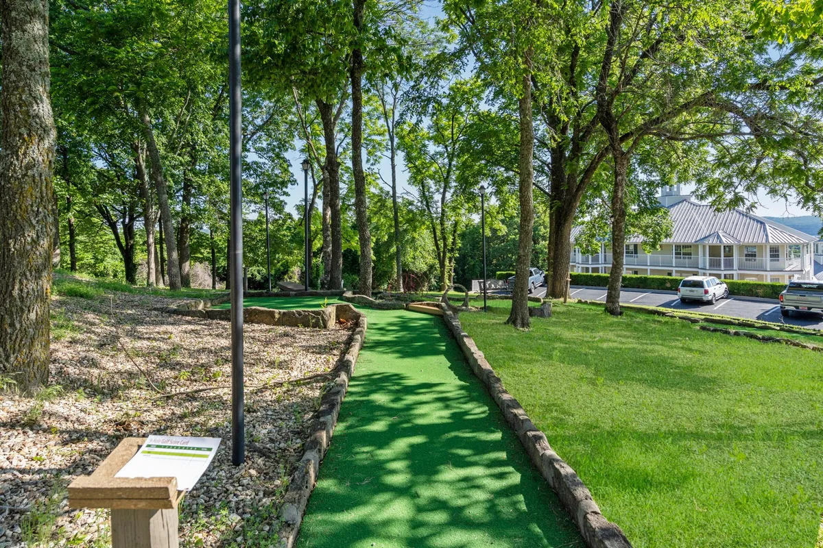 The photo focuses on a playful mini-golf path winding through lush greenery, with clear signage and a serene natural backdrop, suggesting opportunities for friendly competition and laughter.