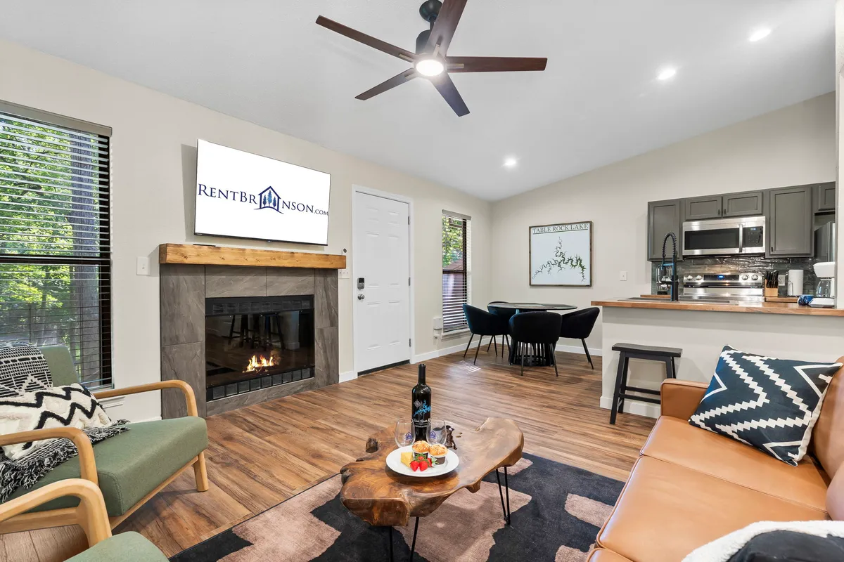 A welcoming open-plan living area featuring a cozy fireplace, a plush sofa, a coffee table, a TV, and a dining table. The arrangement encourages gathering for movie nights, relaxing by the fire, or shared meals and games around the dining table.