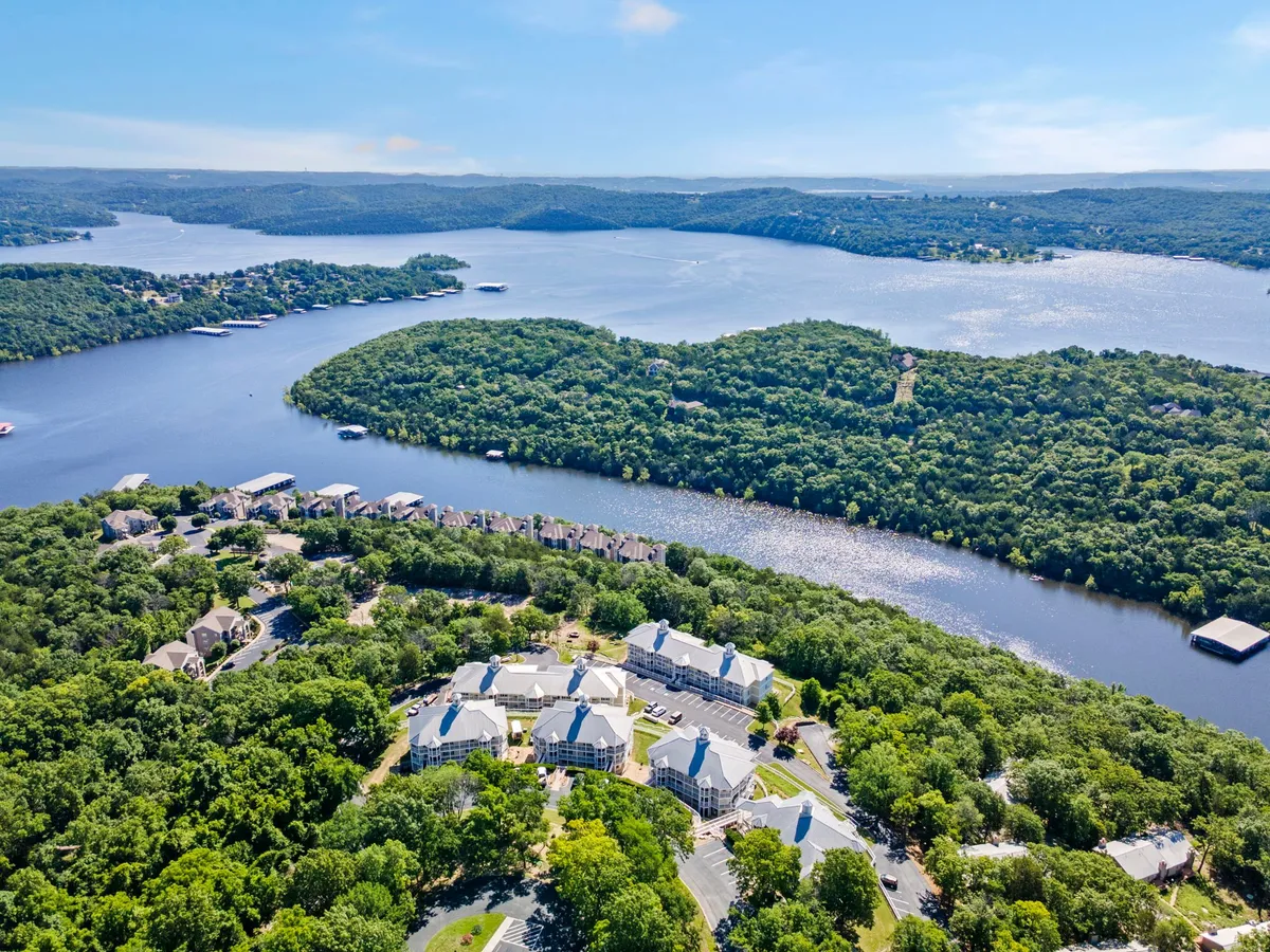 A sweeping view of a winding river surrounded by lush green hills and dotted with residential buildings and boats. The landscape invites exploration, with visible trails and plenty of natural beauty to discover.