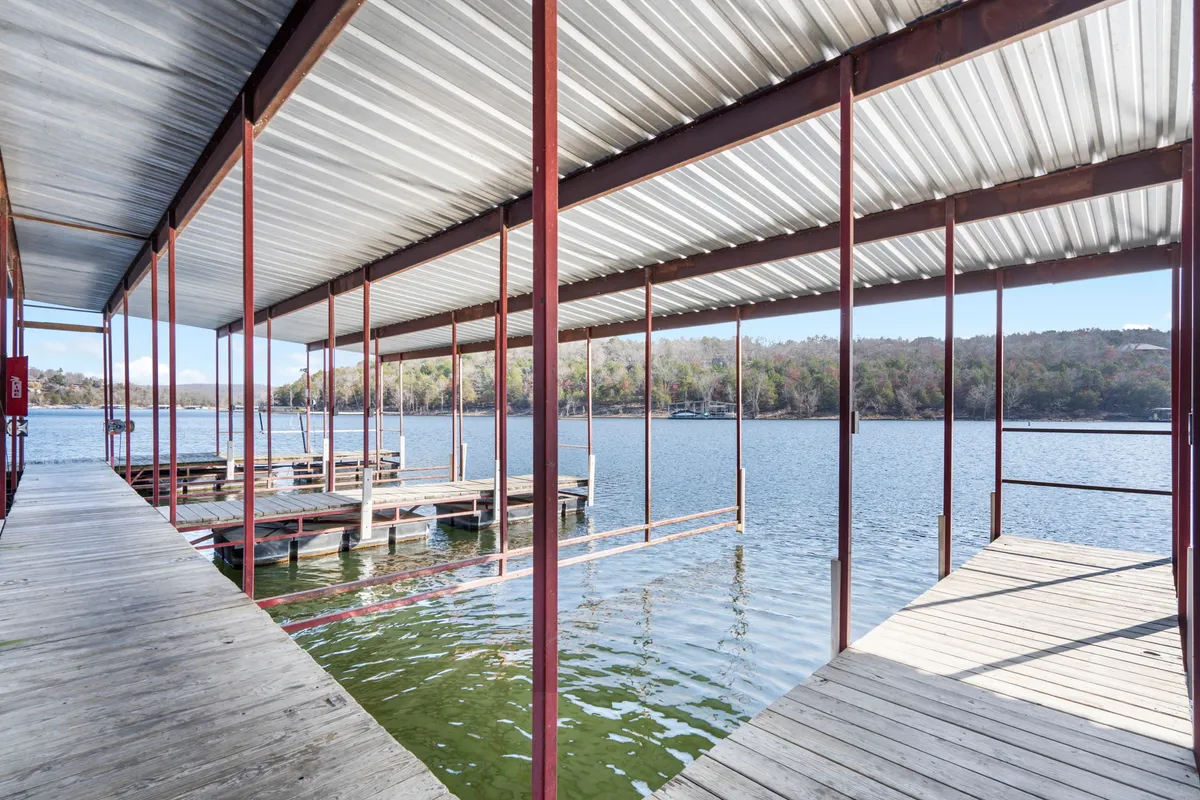 A serene wooden dock extends over the calm water, surrounded by lush foliage. The setting sun paints the water in warm hues, creating an inviting spot for boating, fishing, or simply enjoying nature's beauty.