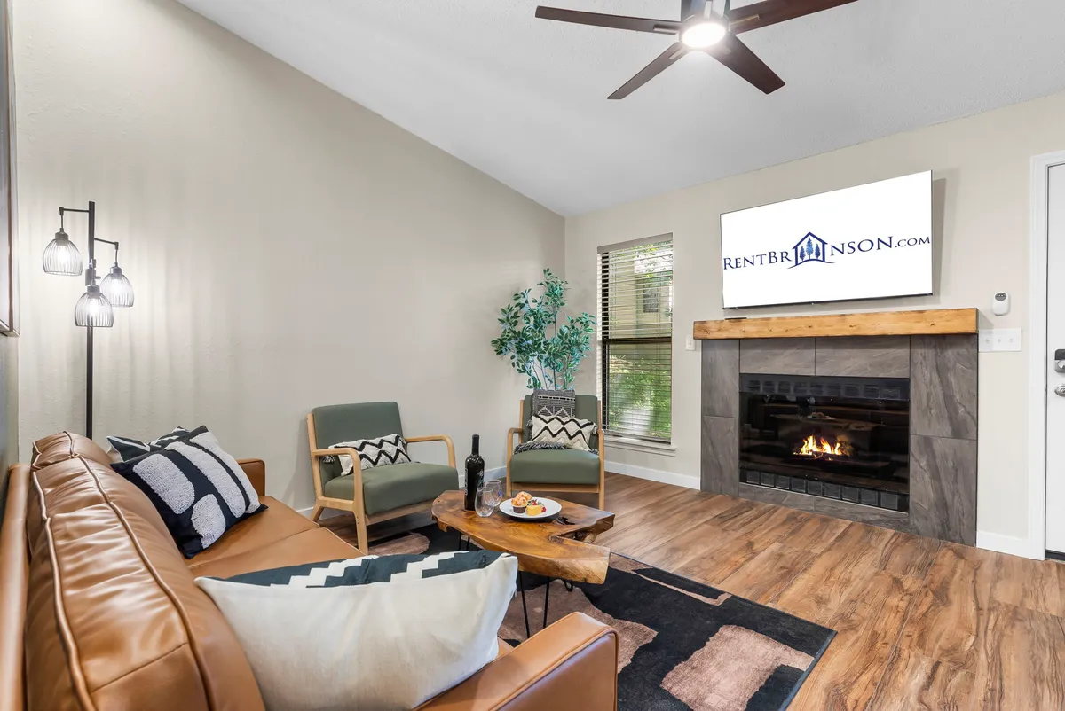 The hero image showcases a stylish living area featuring a plush leather sofa, a glowing fireplace, modern wooden coffee table, lush green plants, and a flat-screen TV. The ambiance is cozy yet contemporary, inviting guests to unwind together or enjoy quiet moments indoors.