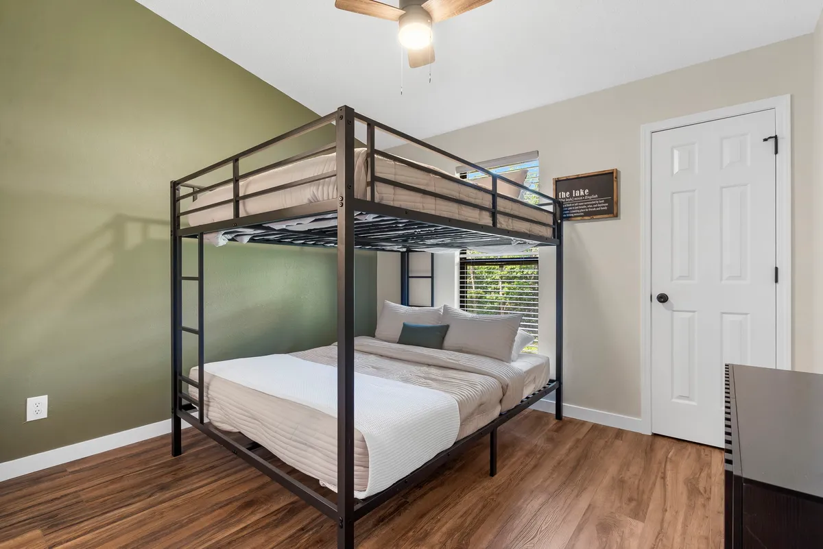 A cozy bedroom with a full-over-full bunk bed, a window letting in natural light, and playful wall decor. The arrangement suggests a welcoming space for kids or friends, perfect for sharing stories and winding down together.